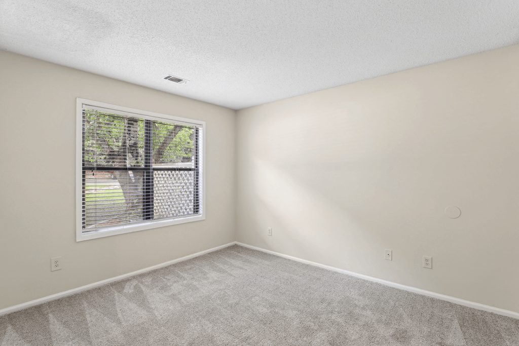an empty bedroom with a large window and carpeting