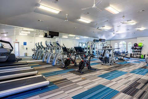 A gym with a variety of exercise equipment including treadmills, stationary bikes, and weight machines.