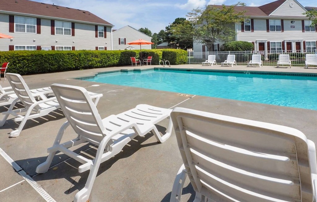 Swimming pool with lounge chairs alongside the pool. Tress in the background
