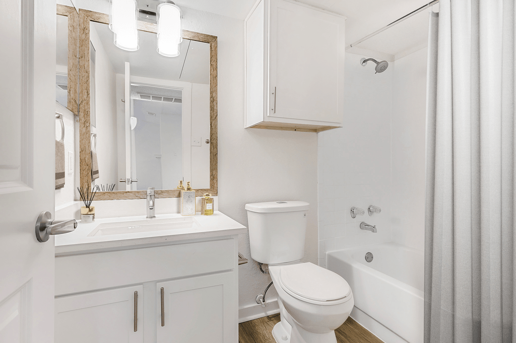 Virtually staged bathroom with white cabinetry, white quartz countertop, custom vanity mirror, medicine cabinet, wood style flooring, sheer shower curtain and toilet