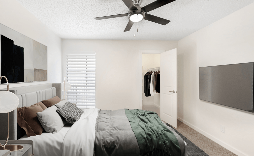 Virtually staged bedroom with carpet, accent rug, wall mounted television, ceiling fan and walk in closet with hanged clothes