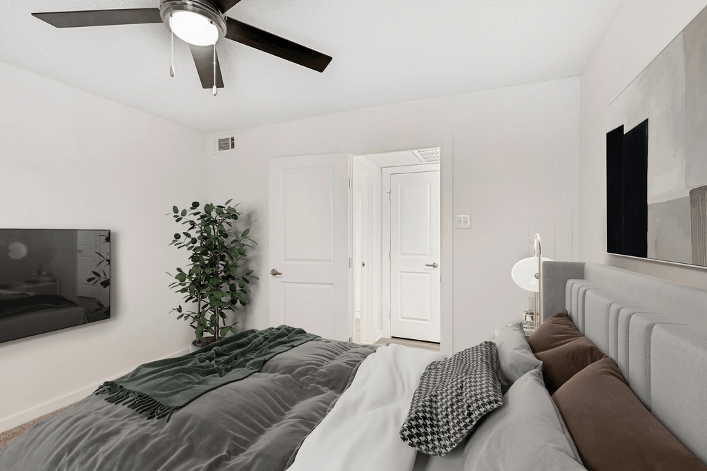 Virtually staged bedroom with wall mounted television, artificial tree, ceiling fan with light and wall art