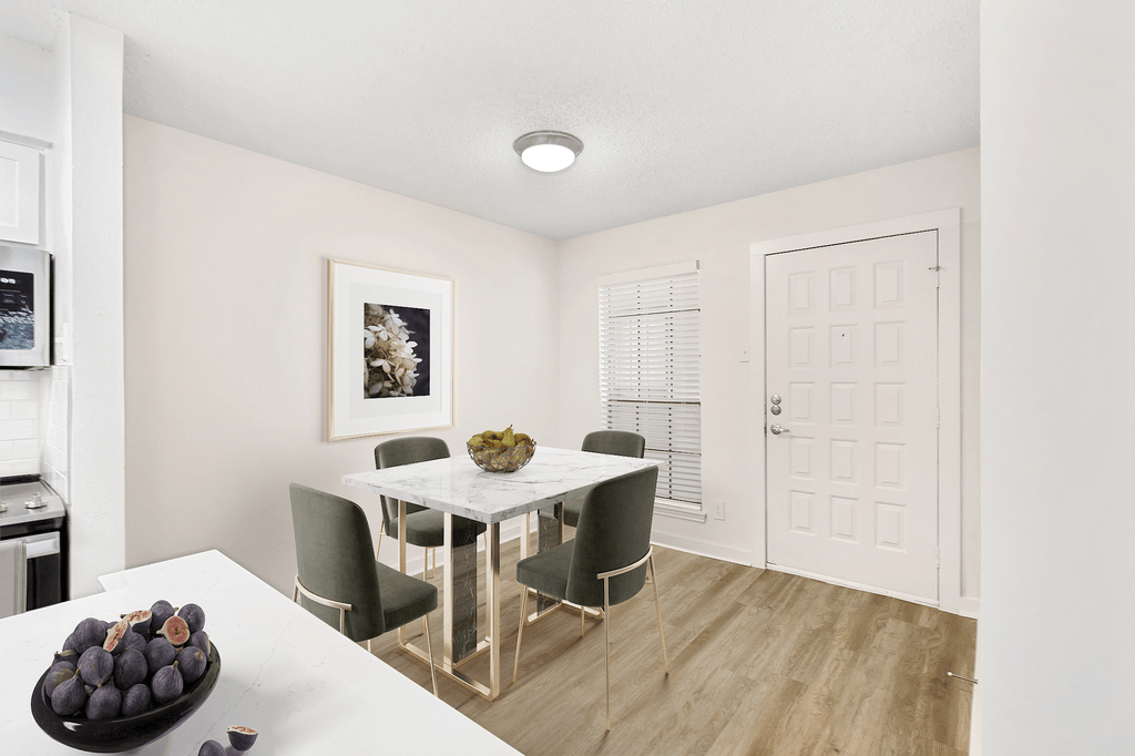 Dining room with square table and chairs, wood style flooring, white quartz countertop in kitchen with fruit bowl and entrance door