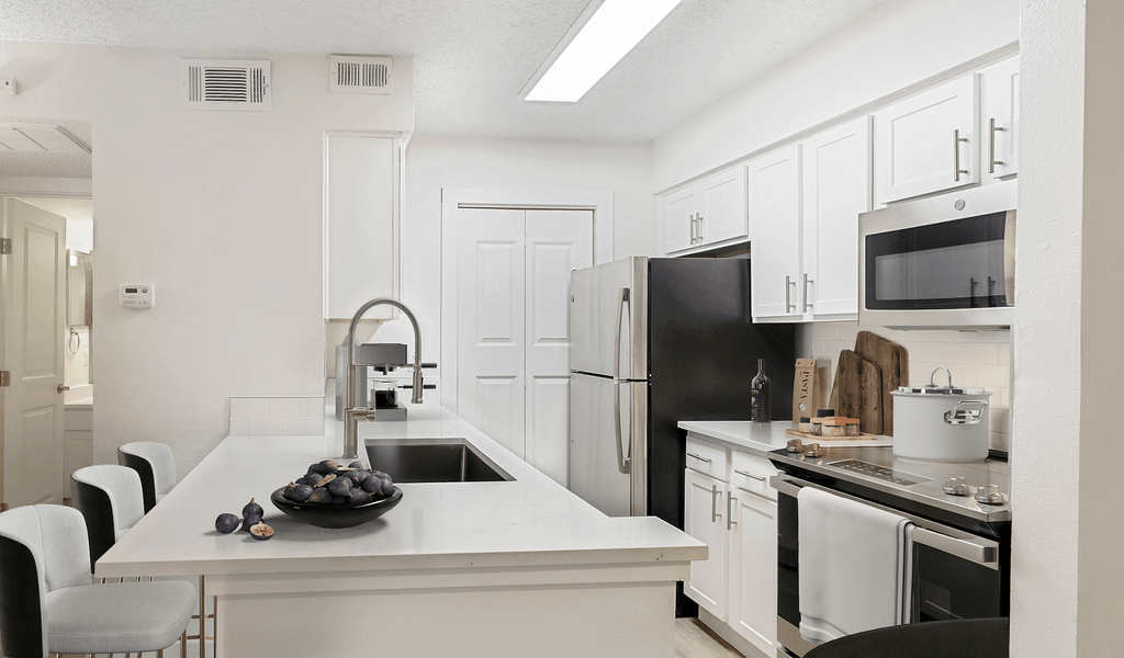 Virtually staged kitchen with white quartz countertops, white cabinetry, stainless appliances, goose neck faucet with sprayer, pot on stove and cutting boards