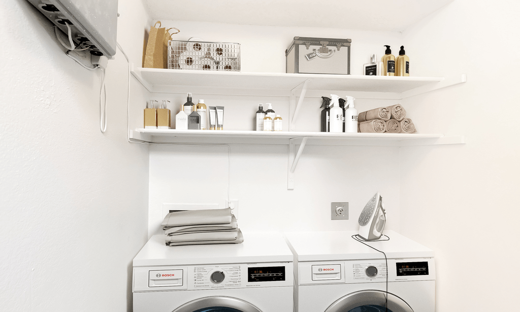 Virtually staged laundry area with washer, dryer, clothes iron, and products on shelves above