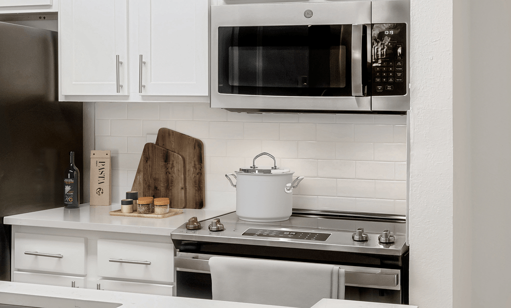 Virtually staged kitchen with stainless appliances, white quartz countertops, white subway tile, white shaker cabinets, pot on stove and cutting boards with spices