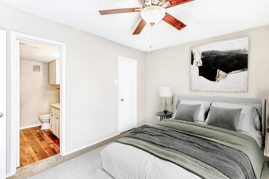 Virtually staged bedroom with carpet, accent rug, bed, nightstand with lamp, ceiling fan with light, en-suite bathroom and closet door
