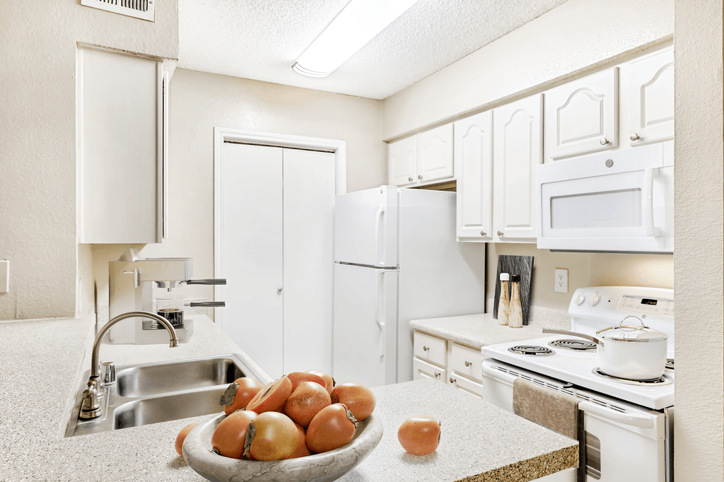 Virtually staged kitchen with granite inspired countertops, white appliances, white cabinetry, coffee machine, pot on stove and fruit bowl