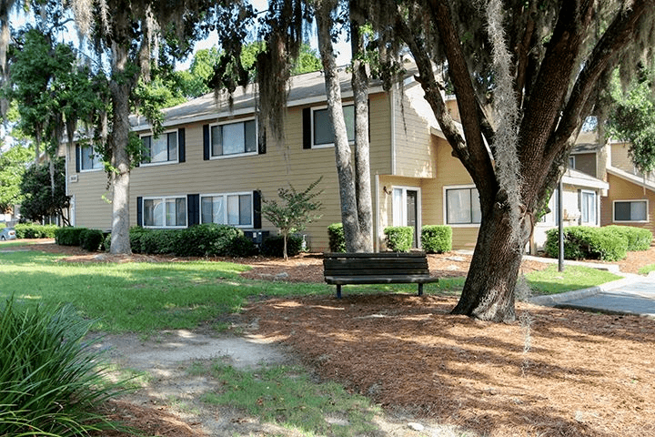 Exterior of buildings with grass and trees and a bench under a tree.