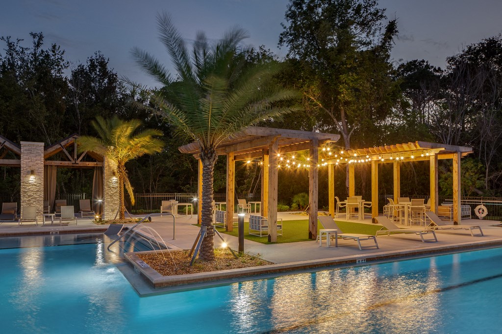 the pool is lit up at night with lights on the pavilion