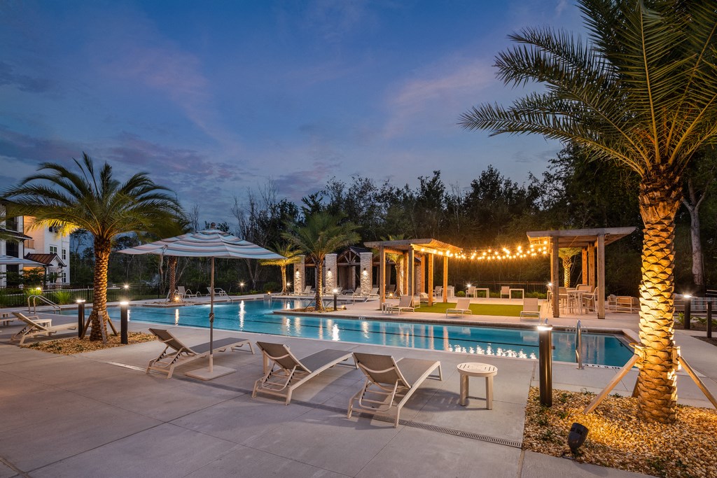 a swimming pool with chairs and palm trees at night