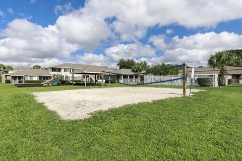A playground with a blue fence and a sandbox in the middle of a grassy area.