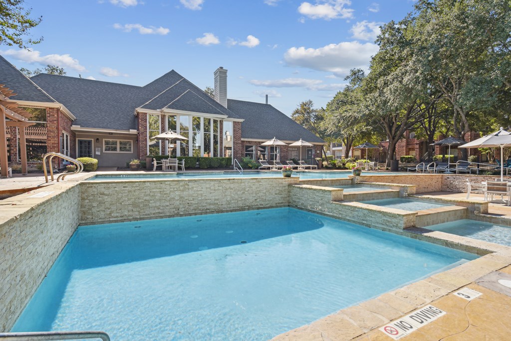 A pool surrounded by a stone wall with a house in the background.