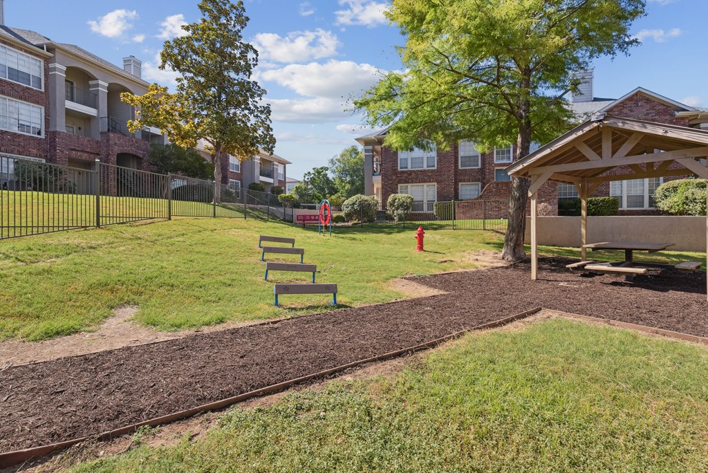 A park area with a dirt path and benches in front of apartment buildings.