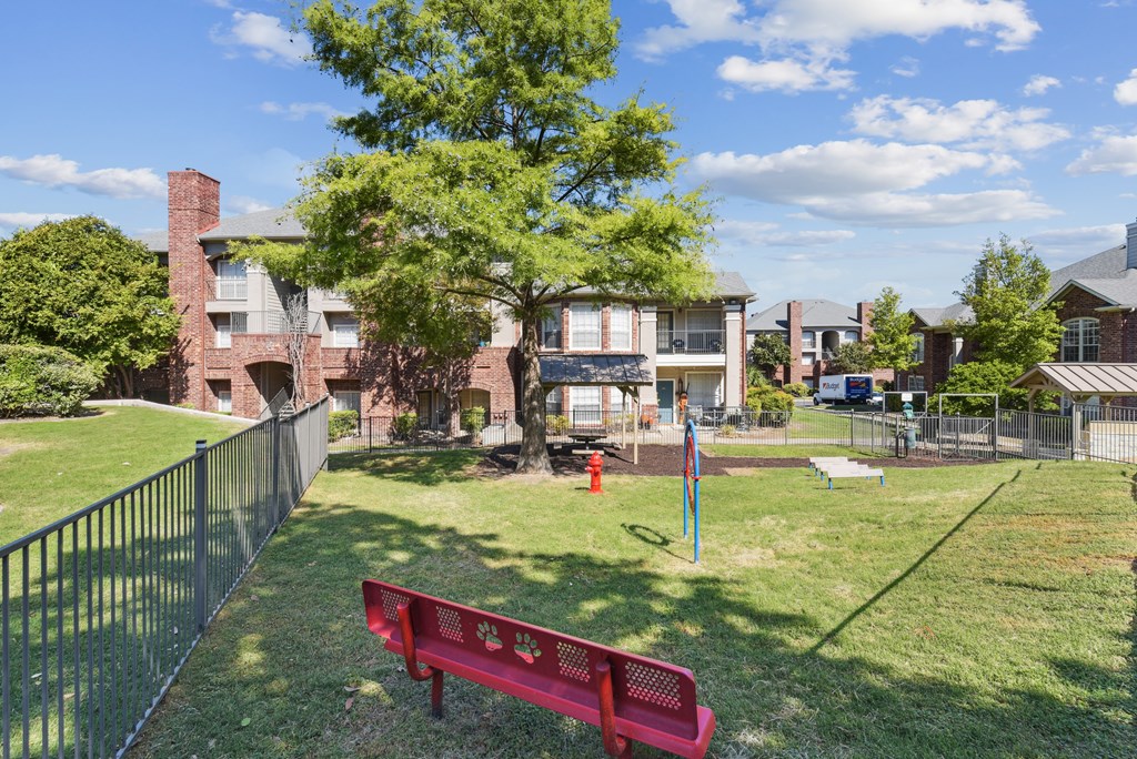A red bench with a logo on it is in the foreground of a grassy area.