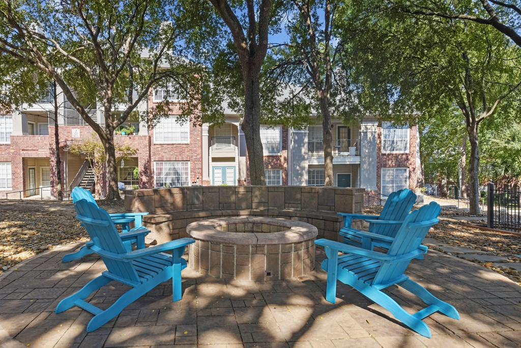 A sunny day at a park with blue chairs and a fire pit.