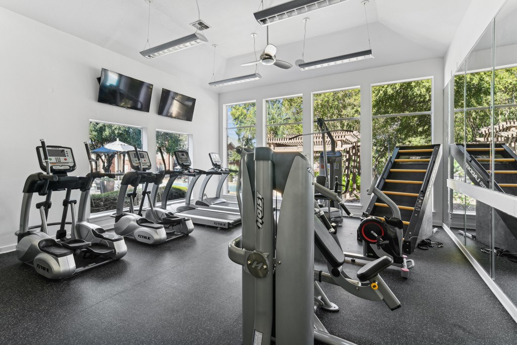 A gym with treadmills, elliptical machines, and a television.
