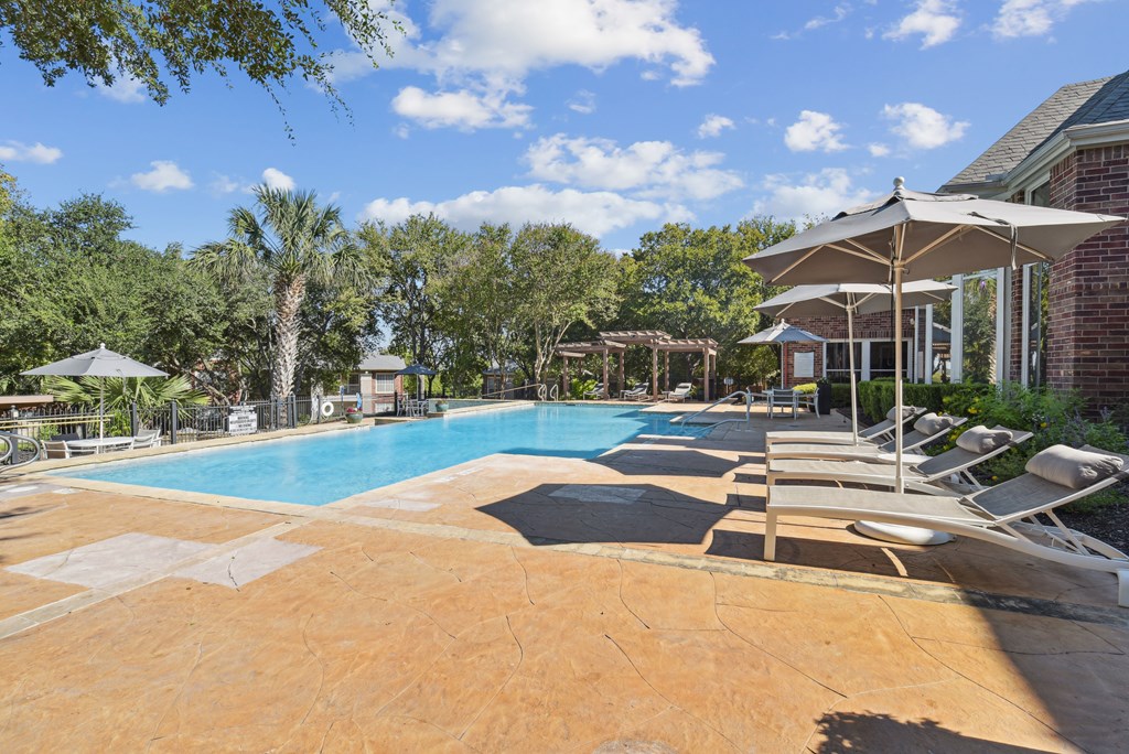 A large outdoor swimming pool surrounded by lounge chairs and umbrellas.