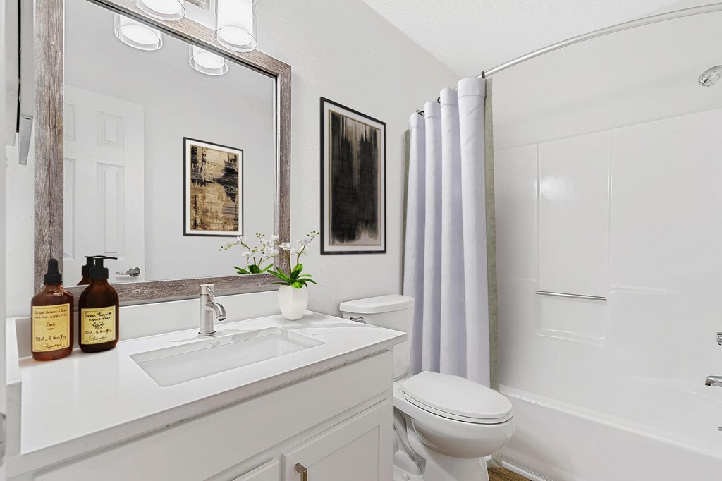 A white bathroom with a toilet, sink, and mirror. at Woodlyn on the Green Apartment Homes, Cary, 27513