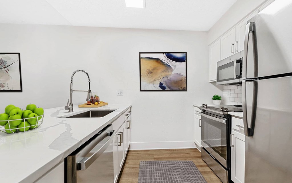A modern kitchen with a white countertop and stainless steel appliances. at Woodlyn on the Green Apartment Homes, Cary, 27513