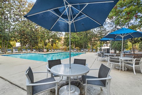 A table with chairs and umbrellas is set up near a pool.