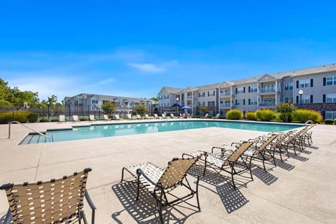A pool surrounded by sun loungers and chairs with apartment buildings in the background.