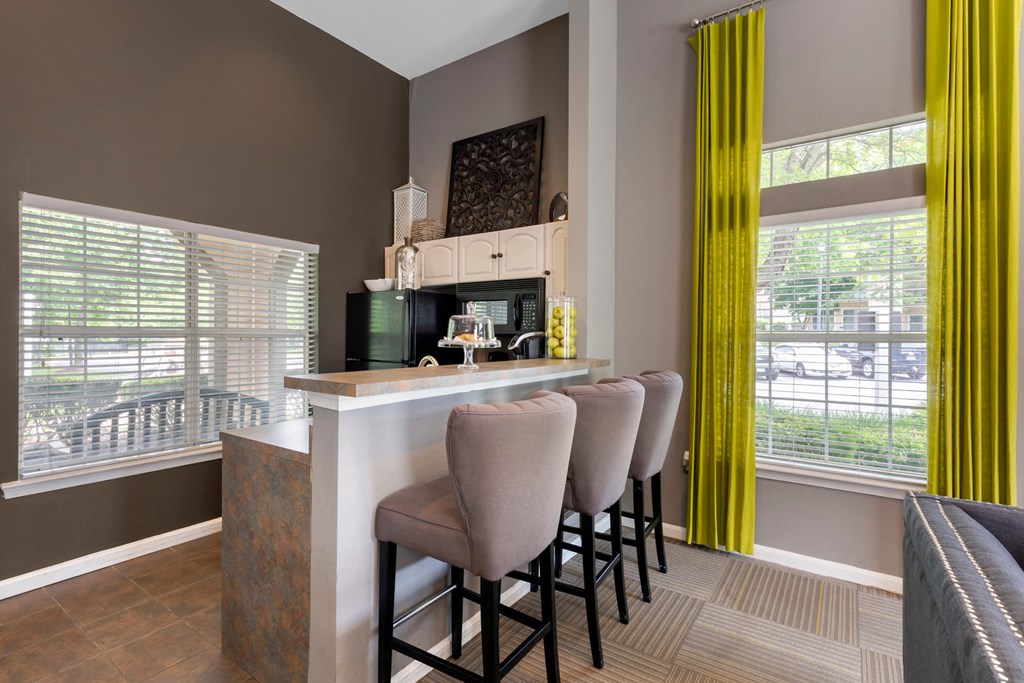 Clubhouse kitchen with 3 gray high top chairs, yellow curtains, tall bar top, black appliances and large open windows