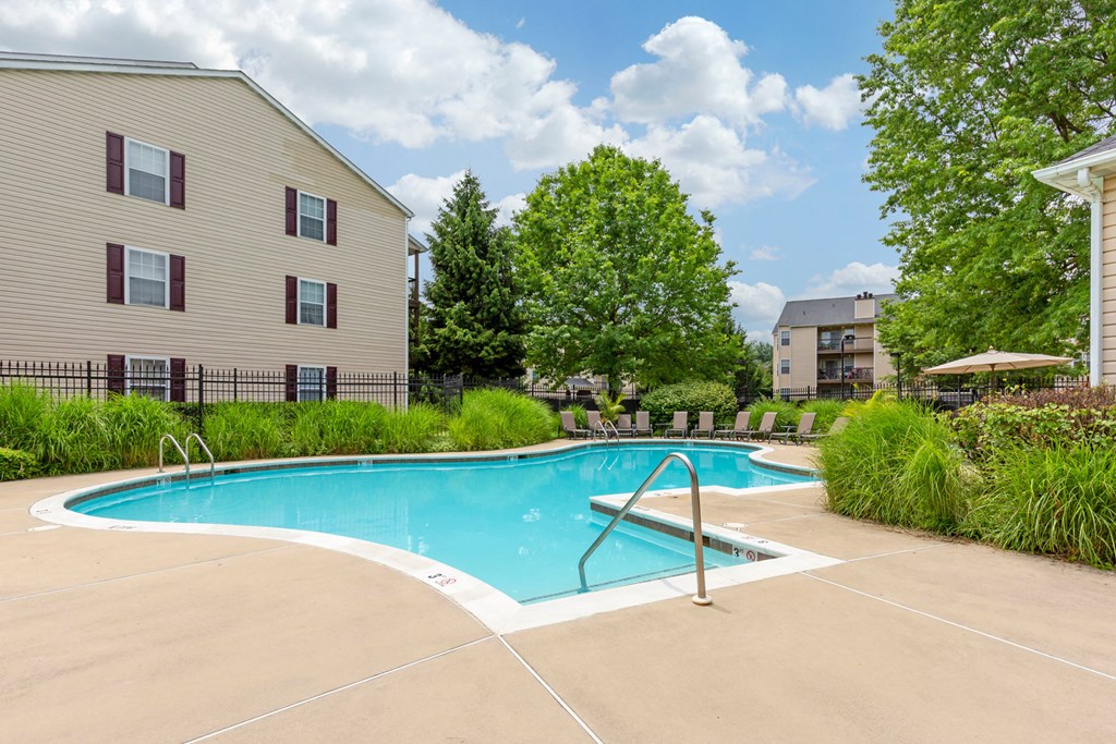 Swimming Pool with sundeck and lounge chairs surrounded by green landscaping and building exteriors