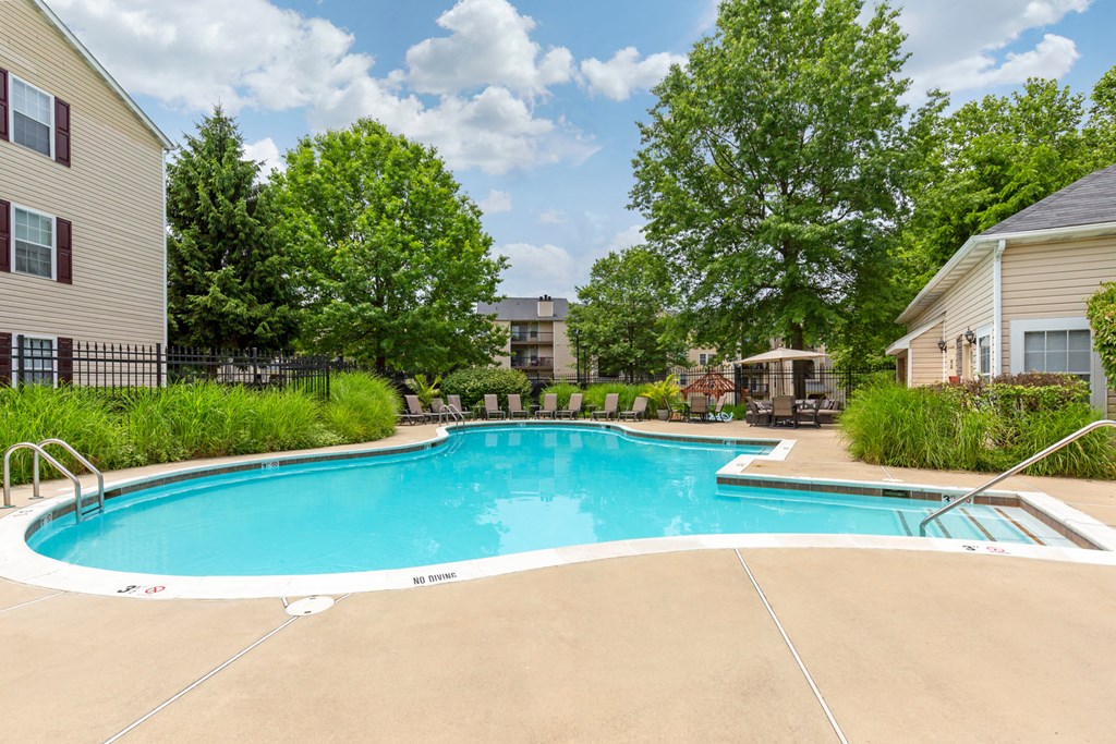 Swimming Pool with sundeck and lounge chairs surrounded by green landscaping and building exteriors
