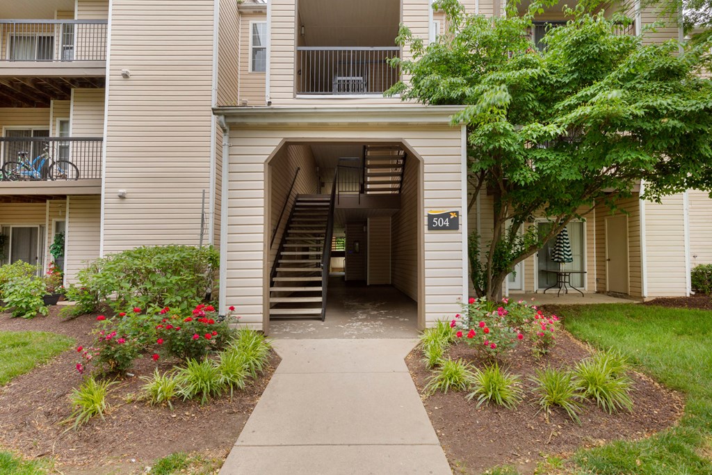 Building exterior with sidewalk, flowers beds with red flowers, mature trees and grass areas