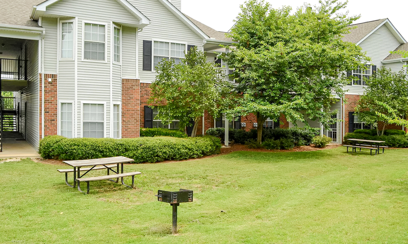 a picnic table and a grill sit in a grassy area in front of an apartment building