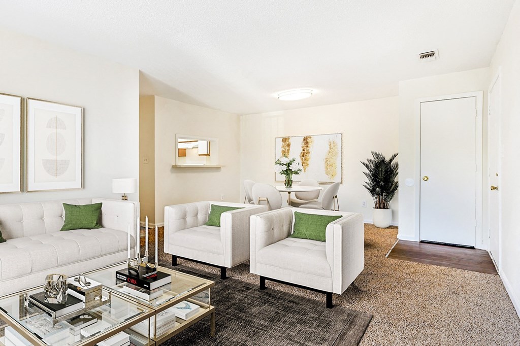 Carpeted living room with a white couch and arm chairs, glass coffee table and dining table set in the background