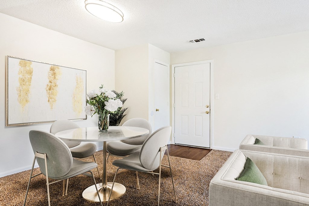 Carpeted living room and dining area with marble table and chair set with art above the wall and view of couches in the back.