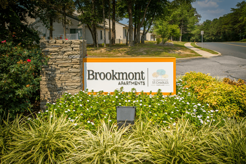 A sign for Brookmont Apartments is surrounded by flowers and greenery.
