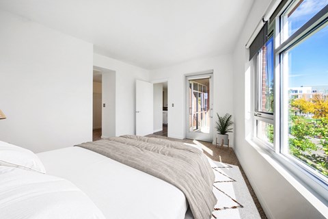 A bedroom with a large bed and a window overlooking a cityscape.