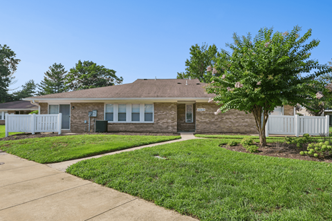 A house with a white picket fence and a tree in front.