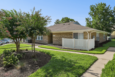 A house with a white fence and a tree with pink flowers in front.