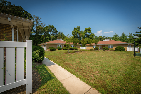 A white picket fence leads to a grassy area with three houses in the background.
