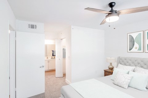 A bedroom with a bed, a ceiling fan, and a nightstand with a lamp.