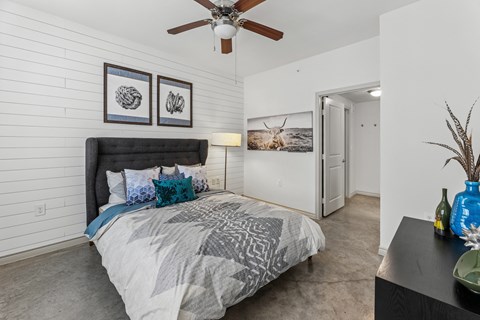 A bedroom with a bed, a ceiling fan, and a painting on the wall.