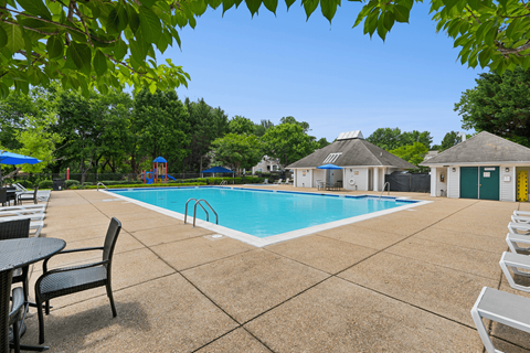 A pool surrounded by a patio with chairs and a table.
