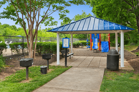 A gazebo with a blue roof is surrounded by trees and has a sign in front of it.