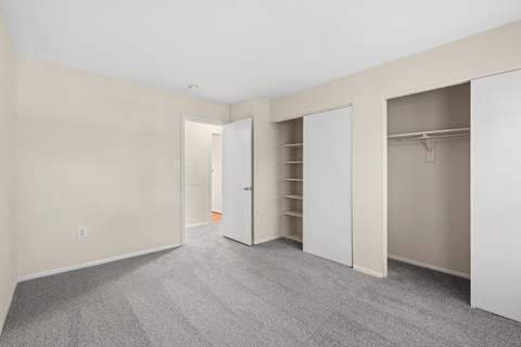 A room with a carpeted floor and white closet doors.