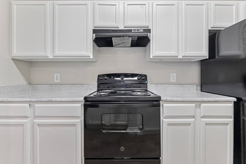 A black stove in a kitchen with white cabinets.