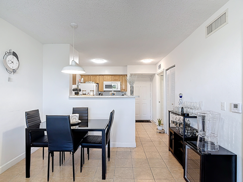 A black dining table with four chairs is in a kitchen with white walls.