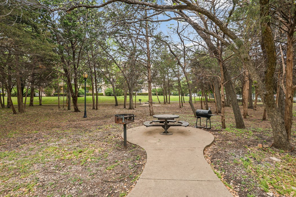 A picnic table sits in the middle of a park with a pathway leading to it.