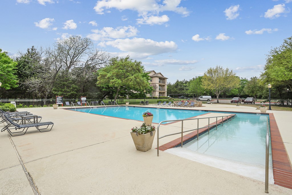 A large outdoor swimming pool surrounded by trees and a building in the background.