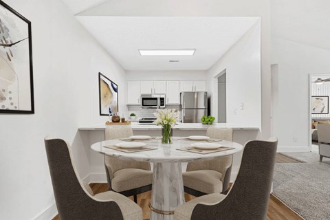 a dining area with a table and chairs and a kitchen in the background