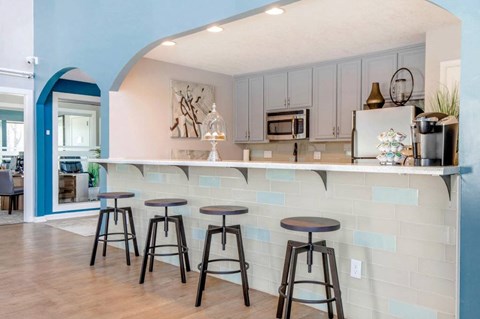 A kitchen with a bar area featuring a white counter and blue tiled backsplash.