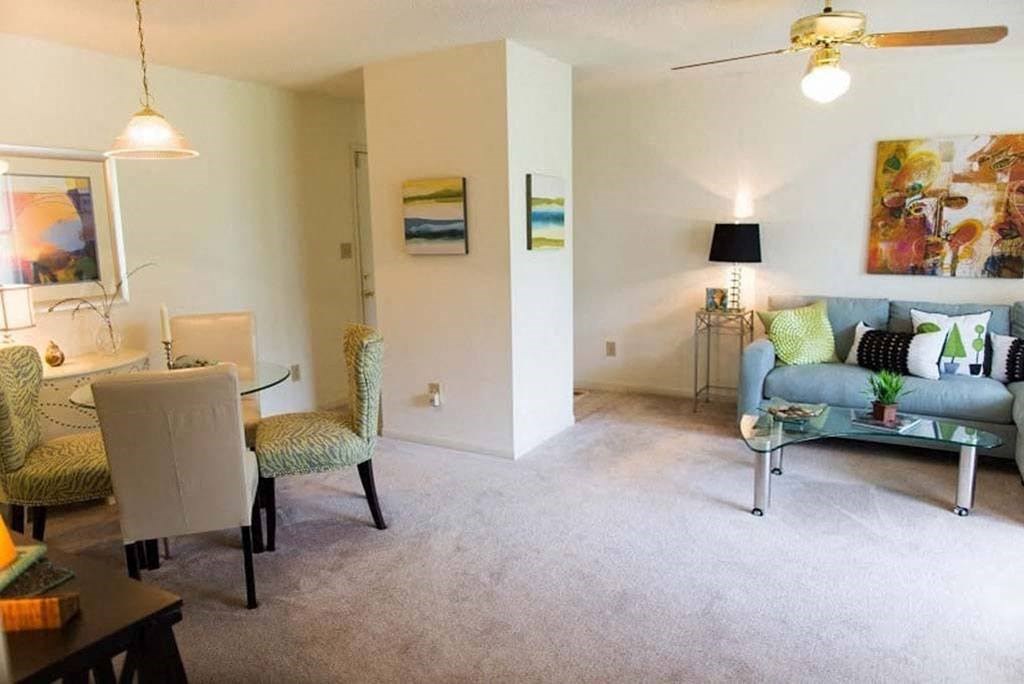 A living room with a grey sofa, a glass table, and a painting on the wall at Fox Hollow Apartment Homes, High Point, NC, 27265